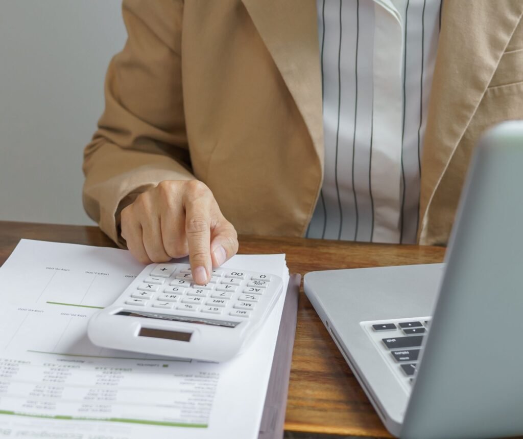 Restaurant manager uses a calculator beside a laptop to review invoices and track rising ingredient costs during a cost spike.