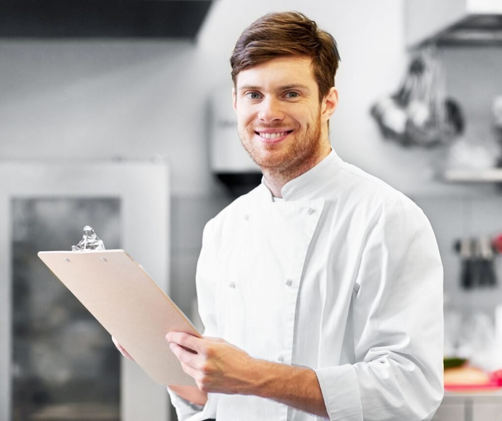 A chef in a professional kitchen reviewing a weekly expense report and inventory checklist on a clipboard.